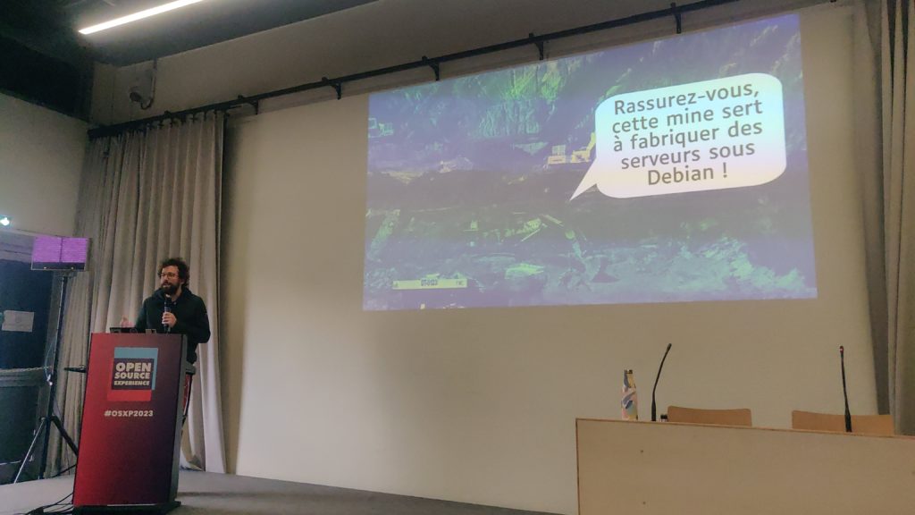 Une photo de la conf, avec une slide qui montre une mine en Afrique, et une bulle qui dit : « Rassuez-vous, cette mine sert à favriquer des serveurs sous Debian ! »